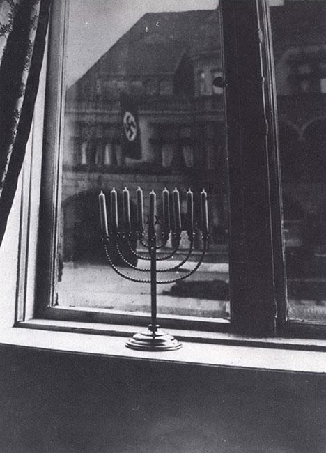 Hanukkah menorah in Kiel, Germany, in a window of a prewar Jewish home with the Nazi banner visible in the background.